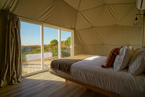 Slaapkamer in Dome House van Wecamp Reserva Alecrim, Portugal, met zicht op terras en groene omgeving.