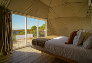 Slaapkamer in Dome House van Wecamp Reserva Alecrim, Portugal, met zicht op terras en groene omgeving.