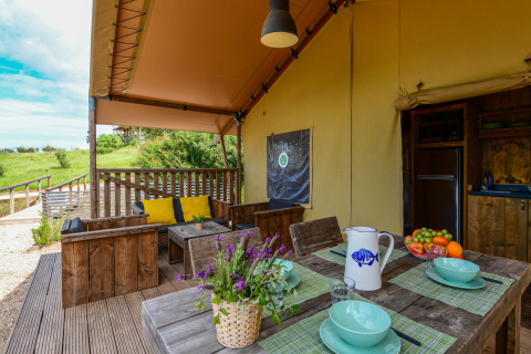 Knus safari tent terras met houten meubels, kleurrijke kussens en vers fruit bij Wecamp Reserva Alecrim in Portugal.