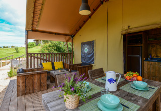 Acogedora terraza de tienda safari con muebles de madera, cojines de colores y fruta en Wecamp Reserva Alecrim.