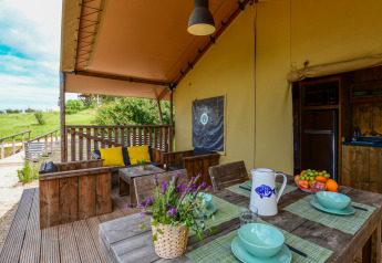 Gemütliche Safari-Zeltdachterrasse mit Holzmöbeln, bunten Kissen und frischem Obst bei Wecamp Reserva Alecrim.