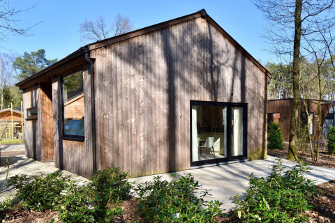 Exterior view of Lysdann lodge featuring wooden siding, large windows, and a forested surrounding landscape.