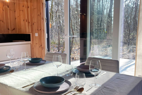 Sunlight fills the dining area at Lysdann lodge in Belgium, with a set table and woodland views.