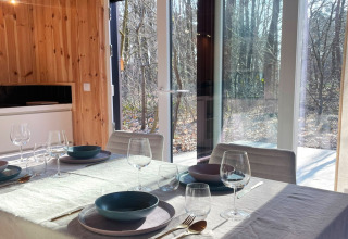 Sunlight fills the dining area at Lysdann lodge in Belgium, with a set table and woodland views.