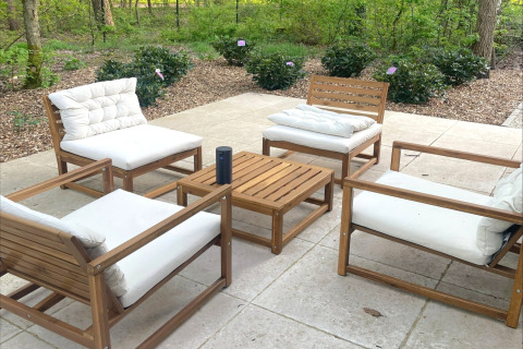 Outdoor seating area with four cushioned wooden chairs and table at Lysdann lodge in Belgium.