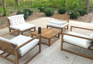 Outdoor seating area with four cushioned wooden chairs and table at Lysdann lodge in Belgium.