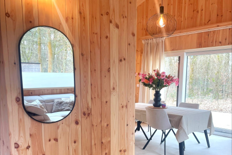 Bright wooden lodge interior with mirror, dining table, and flowers at Lysdann in Belgium.