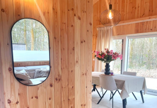 Bright wooden lodge interior with mirror, dining table, and flowers at Lysdann in Belgium.