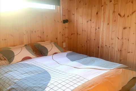 Sunny bedroom with double bed, colorful bedding, and wood-paneled walls at Lysdann lodge in Belgium.