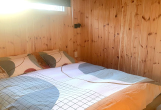 Sunny bedroom with double bed, colorful bedding, and wood-paneled walls at Lysdann lodge in Belgium.