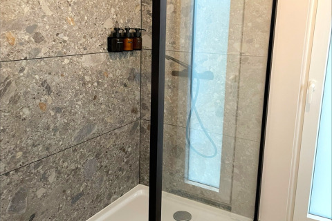 Modern shower booth at Lysdann lodge in Belgium with stone tiles and mounted soap dispensers.
