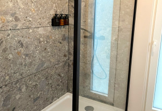 Modern shower booth at Lysdann lodge in Belgium with stone tiles and mounted soap dispensers.