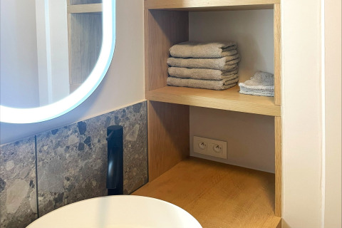 Modern bathroom with wooden shelves, folded towels, LED mirror, and power outlets at Lysdann lodge, Belgium.