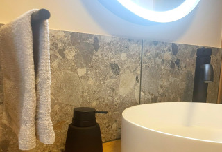 Bathroom scene at Lysdann lodge in Belgium showing a round sink, towel, black soap dispenser and faucet.