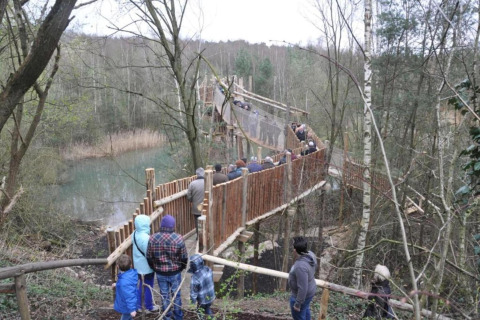 Visitors walk along a wooden hanging bridge near Lysdann lodge in Belgium, crossing over woodland scenery.