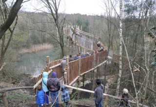 Visitors walk along a wooden hanging bridge near Lysdann lodge in Belgium, crossing over woodland scenery.