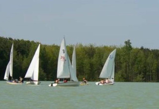 Sailboats on the lake at Lysdann lodge in Belgium, surrounded by trees and under a clear sky.