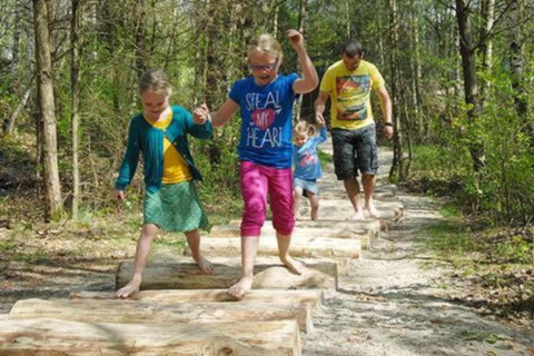 Family walks barefoot on log steps along a nature trail at Lysdann lodge in Belgium, surrounded by trees.