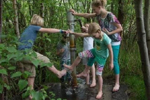 Children having fun barefoot at a water pump in the forest near Lysdann lodge in Belgium.
