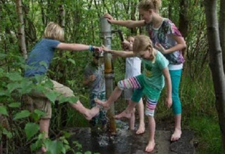 Children having fun barefoot at a water pump in the forest near Lysdann lodge in Belgium.
