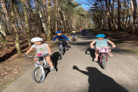 Children riding bikes on a forest path near the Lysdann lodge in Belgium, wearing helmets in sunny weather.