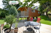Casa móvil 'Manureva' en Bélgica, rodeada de árboles, terraza de madera y muebles de jardín modernos.