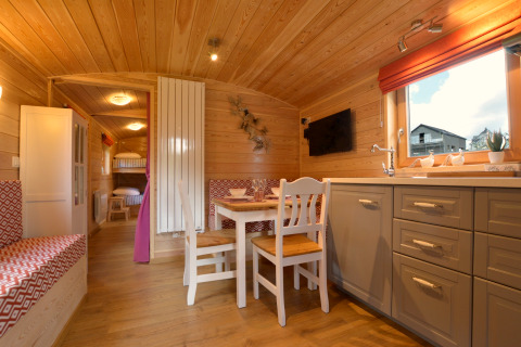 Acogedor interior con paneles de madera del mobil home Manureva en Bélgica, mesa comedor y literas.