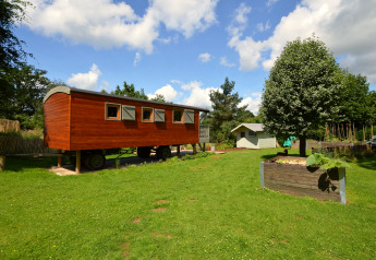 La casa móvil Manureva en Bélgica, ubicada en un césped verde con árboles, cobertizo y jardinera bajo el cielo azul.