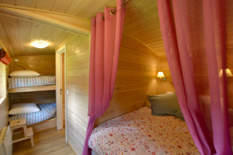 Interior de la casa móvil Manureva en Bélgica con literas, cama doble y cortinas rosas.