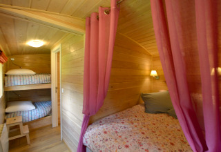Interior de la casa móvil Manureva en Bélgica con literas, cama doble y cortinas rosas.