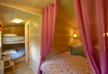 Interior de la casa móvil Manureva en Bélgica con literas, cama doble y cortinas rosas.