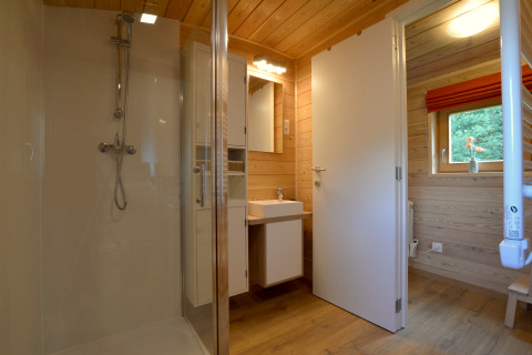 Baño moderno con paneles de madera, ducha y ventana en la casa móvil Manureva en Bélgica.