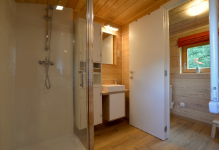 Baño moderno con paneles de madera, ducha y ventana en la casa móvil Manureva en Bélgica.