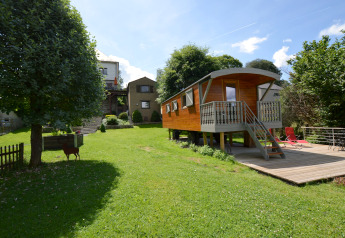 La casa móvil 'Manureva' en Bélgica, situada en un jardín verde con árboles y cielo soleado de fondo.