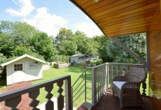 Vista desde el balcón del mobil home Manureva en Bélgica con jardín, cobertizos y silla de mimbre.