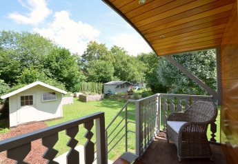 Vista desde el balcón del mobil home Manureva en Bélgica con jardín, cobertizos y silla de mimbre.