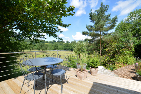 Terraza con mesa redonda, cuatro sillas y macetas en la casa móvil Manureva en Bélgica, vista verde.