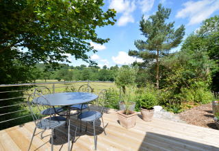 Terraza con mesa redonda, cuatro sillas y macetas en la casa móvil Manureva en Bélgica, vista verde.