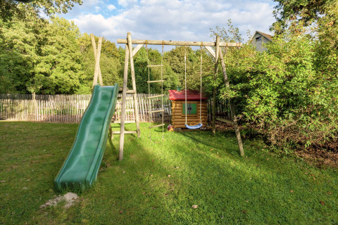 Parque infantil con tobogán, columpio y casita de juegos junto a la casa móvil Manureva en Bélgica.