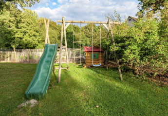 Parque infantil con tobogán, columpio y casita de juegos junto a la casa móvil Manureva en Bélgica.