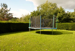 Jardín con una cama elástica en la casa móvil 'Manureva' en Bélgica, rodeado de setos y árboles verdes.