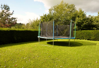 Jardín con una cama elástica en la casa móvil 'Manureva' en Bélgica, rodeado de setos y árboles verdes.