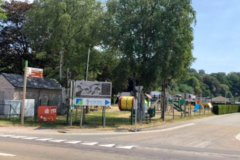 Imagen del mobil home Manureva en Bélgica, con parque infantil, carteles informativos y árboles verdes.