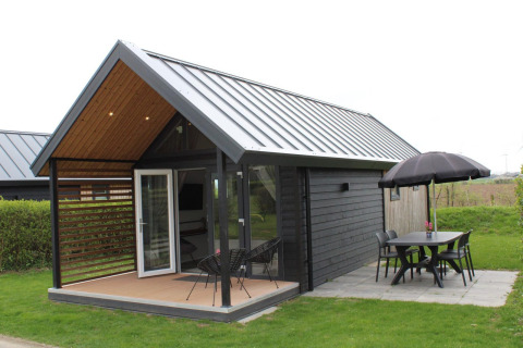 Summer Lodge al Rhederlaagse Meren, Paesi Bassi, con patio, tavolo, sedie e ombrellone nero.