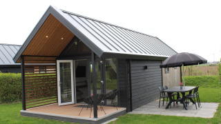 Summer Lodge al Rhederlaagse Meren, Paesi Bassi, con patio, tavolo, sedie e ombrellone nero.