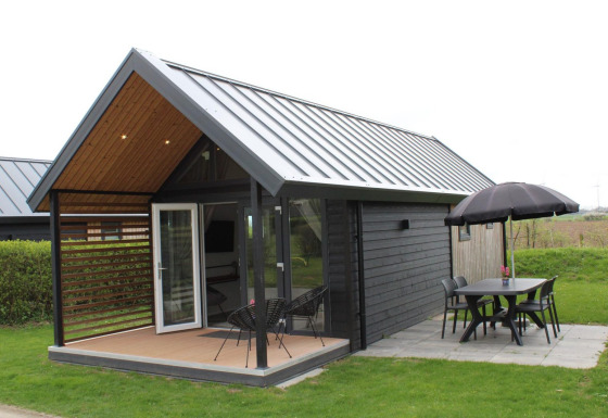 Summer Lodge al Rhederlaagse Meren, Paesi Bassi, con patio, tavolo, sedie e ombrellone nero.