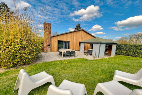 Vue extérieure du lodge Ard Zen en Belgique avec pelouse, terrasse, chaises et façade en bois moderne.