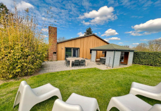 Vue extérieure du lodge Ard Zen en Belgique avec pelouse, terrasse, chaises et façade en bois moderne.