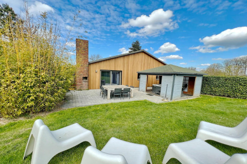 Outdoor view of Ard Zen lodge in Belgium with lawn, patio seating, modern wood siding, and blue sky.