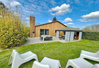 Outdoor view of Ard Zen lodge in Belgium with lawn, patio seating, modern wood siding, and blue sky.